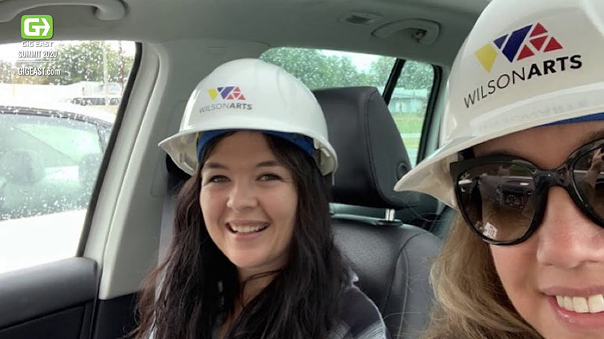 Video still of two smiling women wearing hard hats sitting in a car