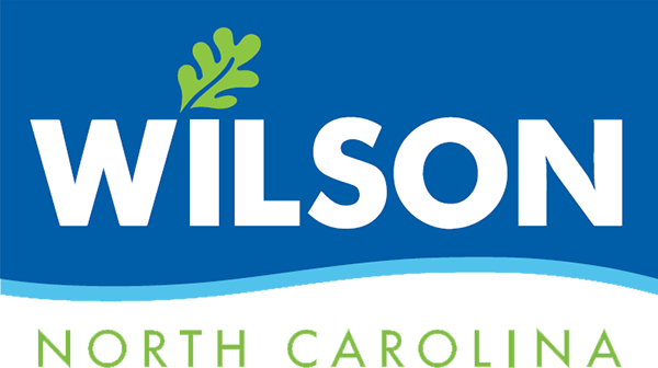 Wilson NC Logo - White sans-serif type with green leaf above on wavy blue background with green sans-serif type below