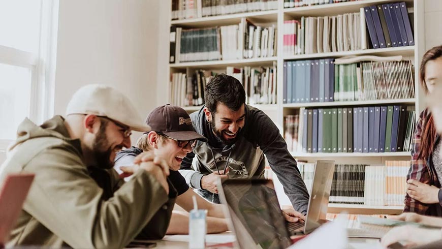 Photo of a group of men laughing while watching something on a laptop