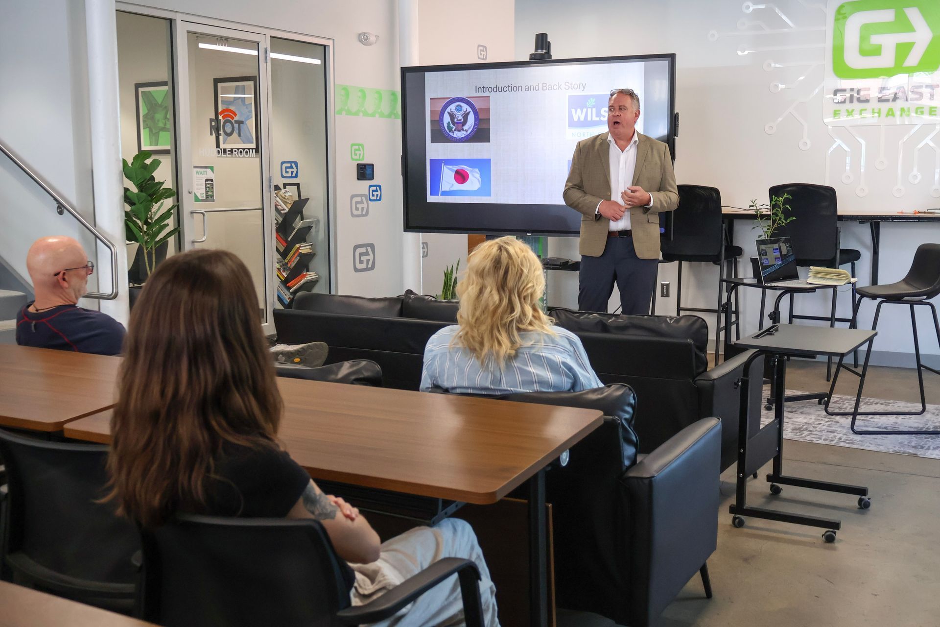 Group of people looking at man in tan suit who is presenting in front of the room